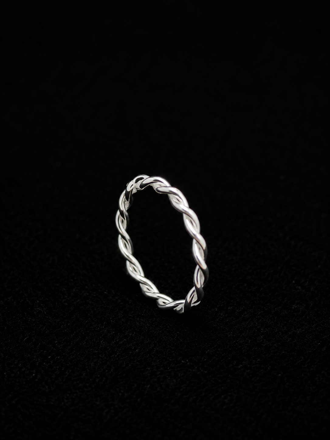 A silver ring with a twisted design on a plain background