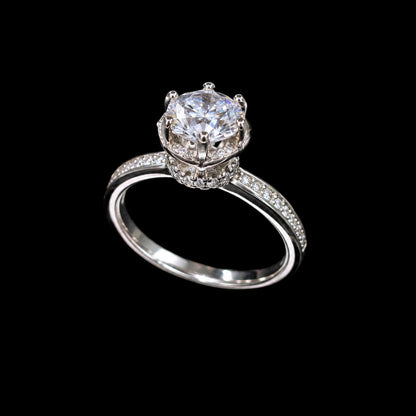 A silver-tone ring with a large clear cubic zirconia stone set in a crown design, surrounded by smaller stones.
