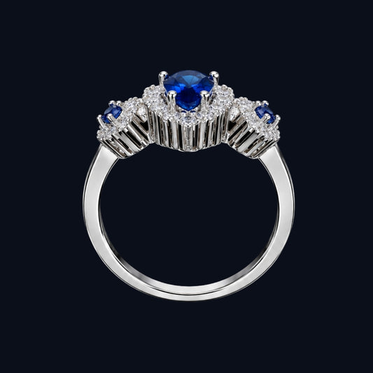 A silver tone ring with a blue CZ stone at its center, surrounded by smaller white CZ stones.