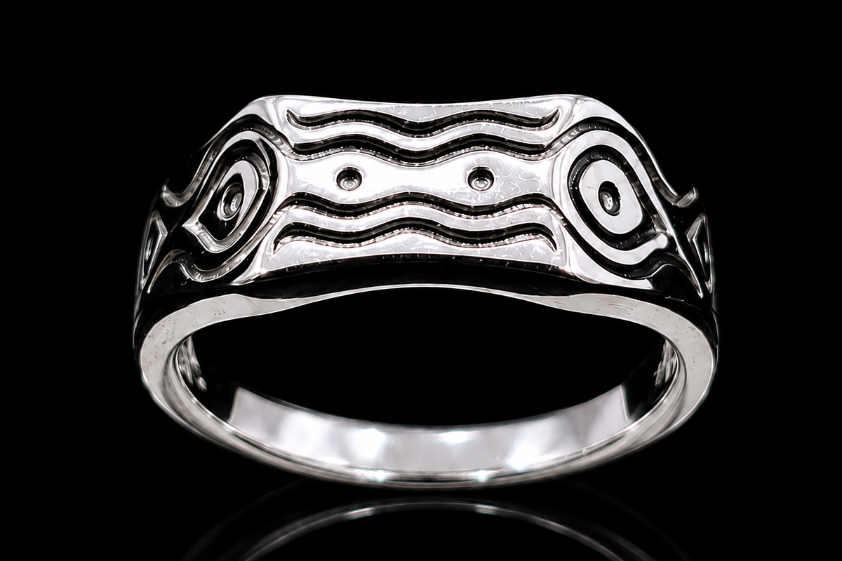 A silver ring with an engraved design on a reflective surface