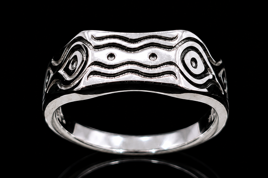 A silver ring with an engraved design on a reflective surface