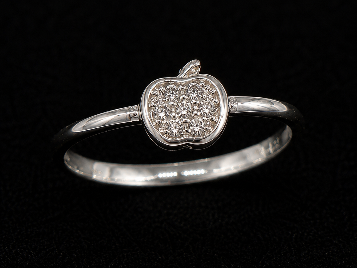 A silver ring with an apple motif and CZ stones, set against a dark background.