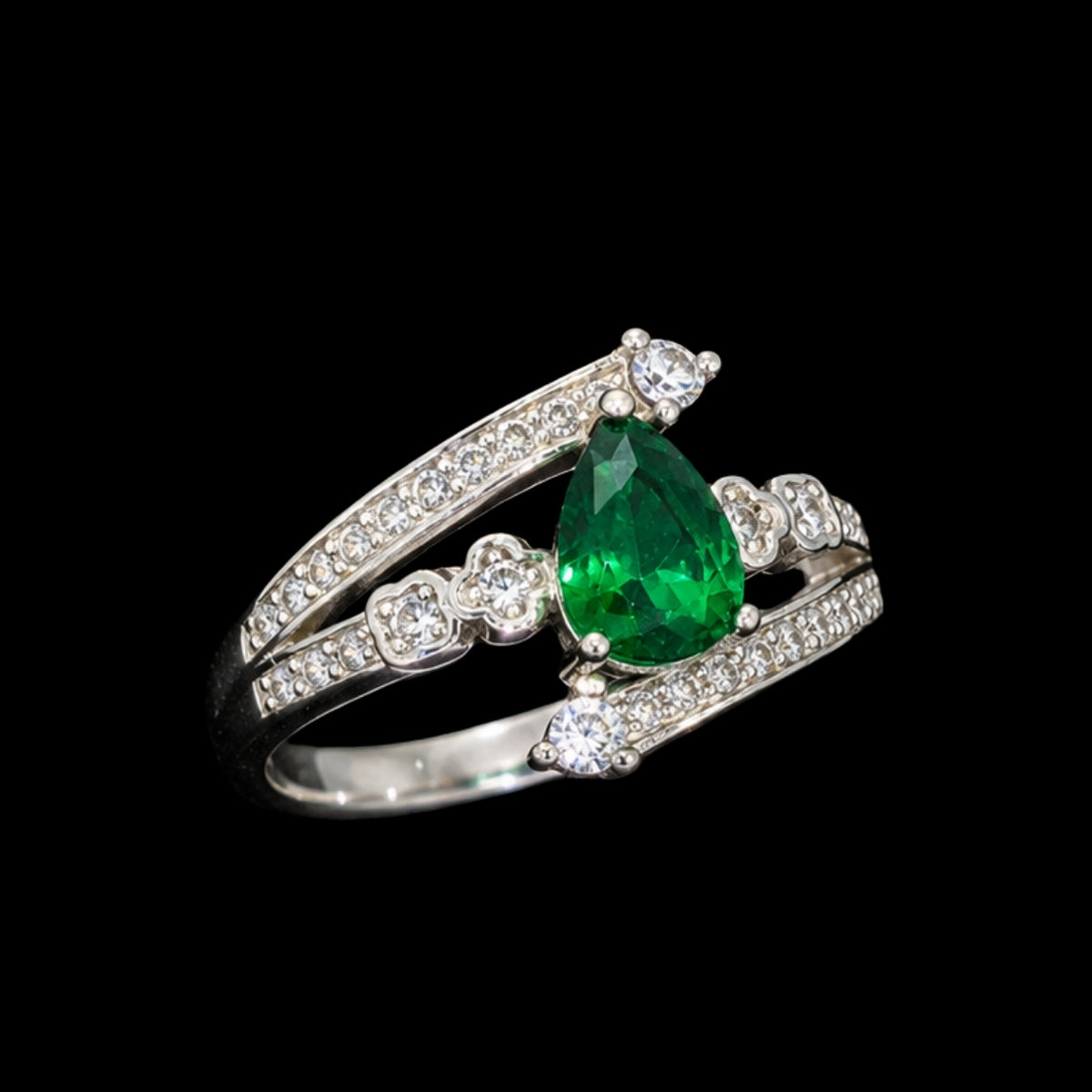 A silver ring with an emerald teardrop stone and floral design.