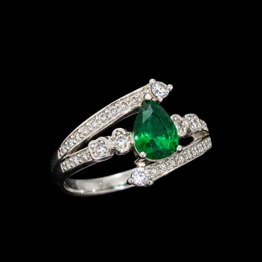 A silver ring with an emerald teardrop stone and floral design.
