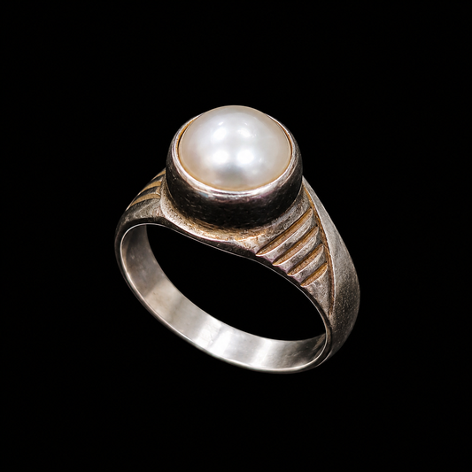 A silver ring with a pearl at its center, set against a neutral background.