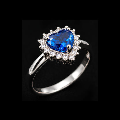 A silver-tone ring with a blue heart-shaped gemstone surrounded by clear gemstones.