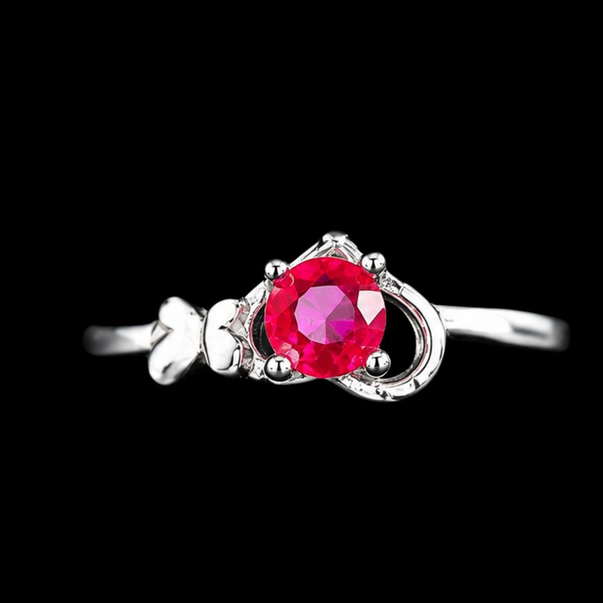 A silver ring with a pink gemstone in the center, set against a dark background.