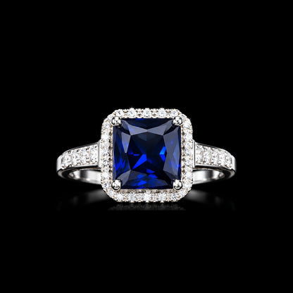 A silver-tone ring featuring a large blue square-cut CZ stone surrounded by smaller clear CZ stones.