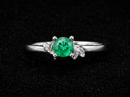 A silver ring with a round-cut green gemstone on a black background