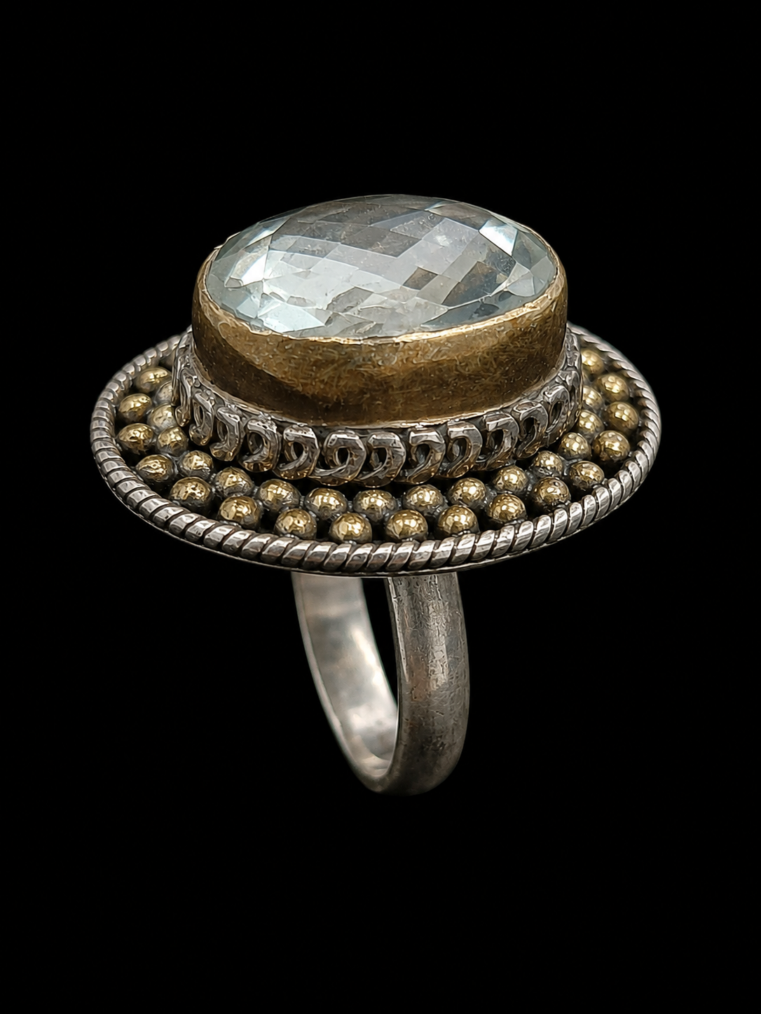 A ring with an oval aquamarine stone, set in silver and gold-tone metal, on a black background.