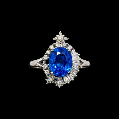 A silver ring with a large blue oval-cut CZ stone and smaller round-cut stones surrounding it, with a star-shaped motif at the top.