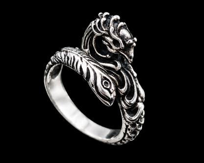 A silver ring with a dragon design on a plain background.