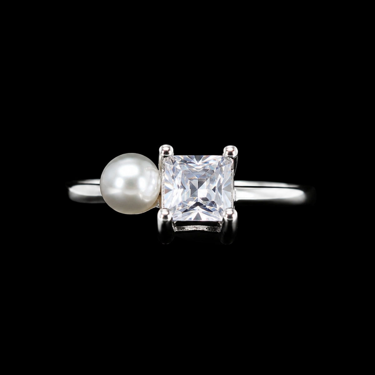 A silver ring with a pearl and a cubic zirconia stone on a black background