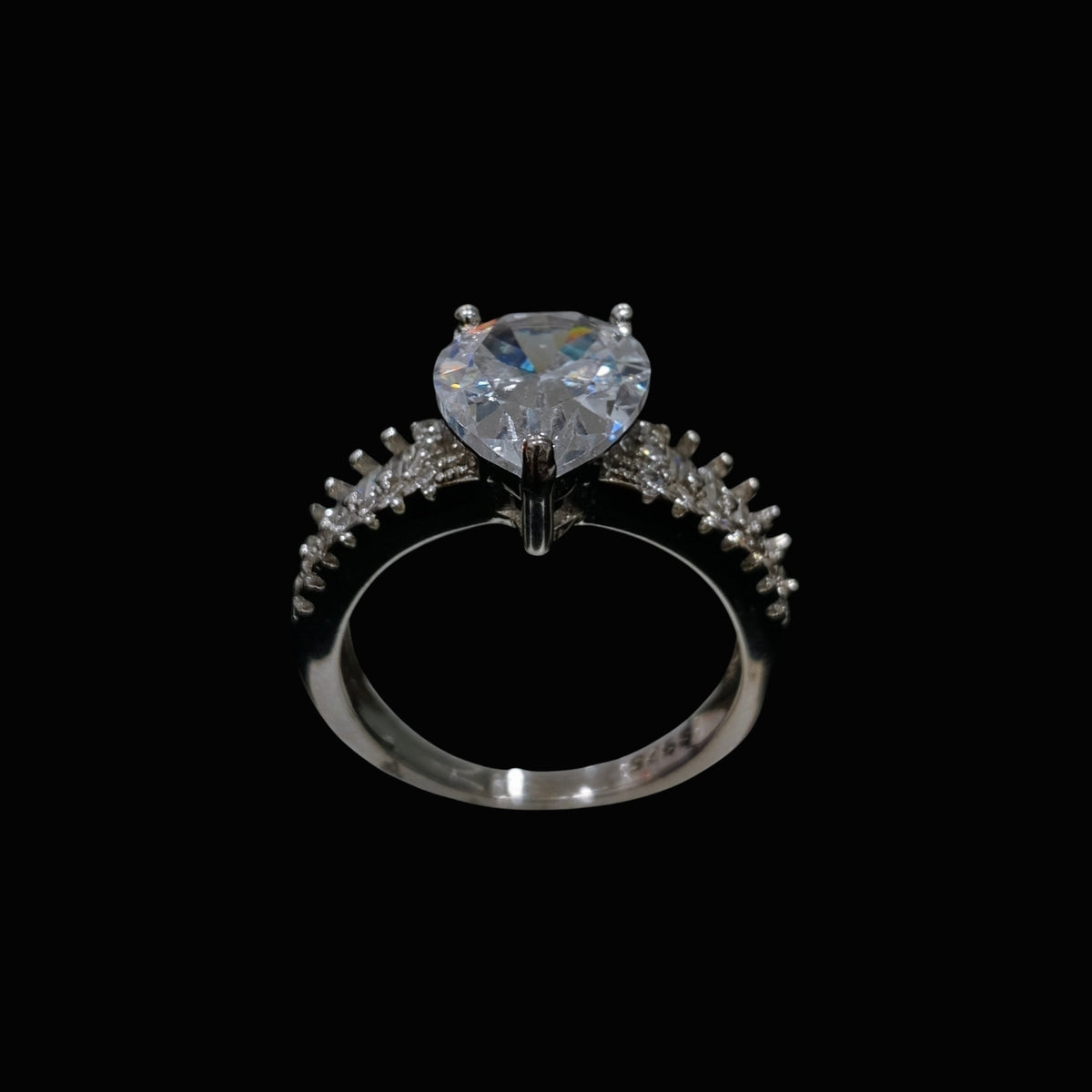 A silver ring with a heart-shaped CZ stone and smaller stones around it, set against a black background.
