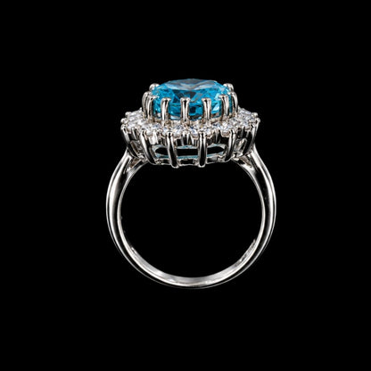 A silver ring with a large blue gemstone in the center, set against a gray background.