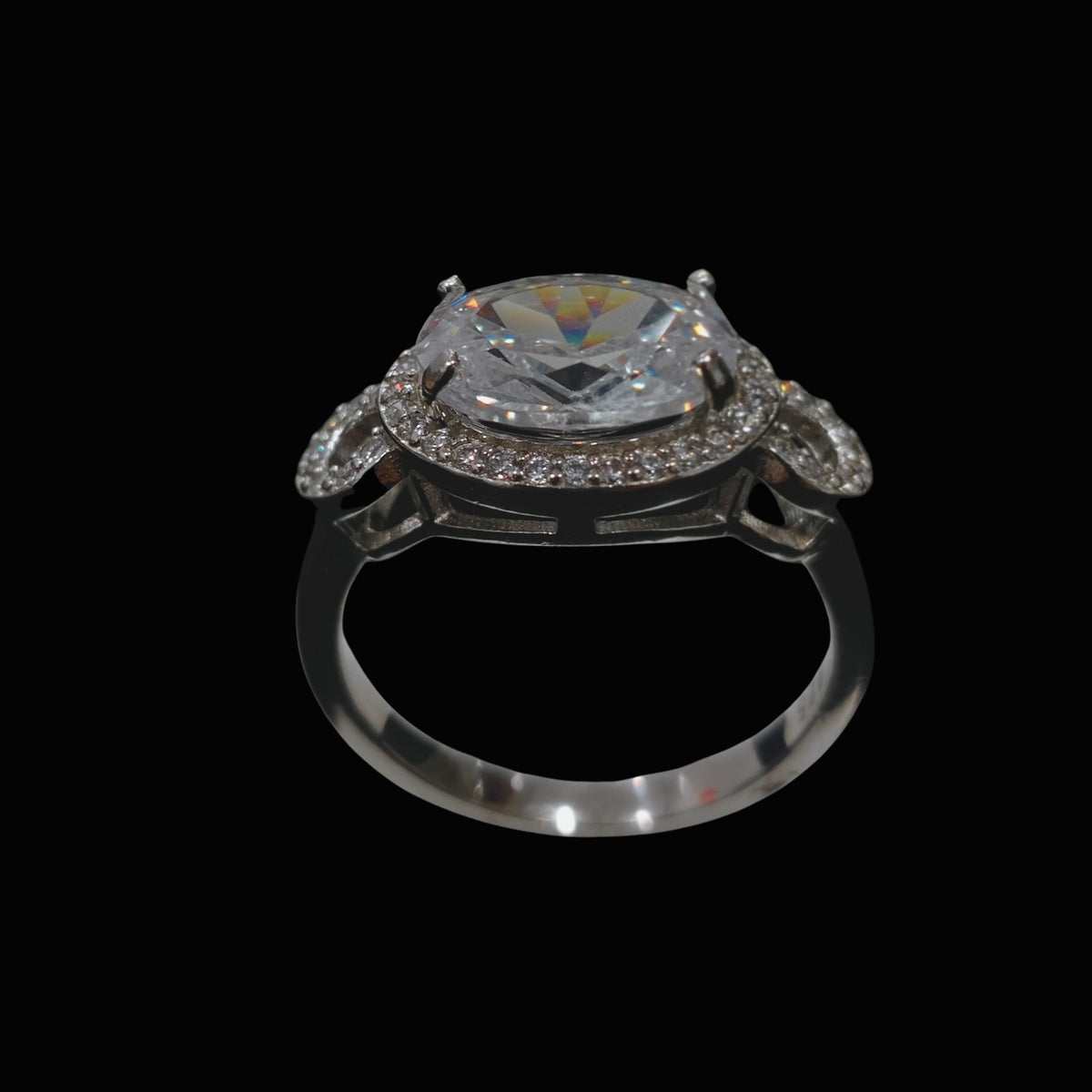 A silver ring with a large clear CZ stone and smaller stones around it, set against a dark background.