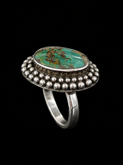A silver ring with an oval turquoise stone and decorative border of small silver balls.