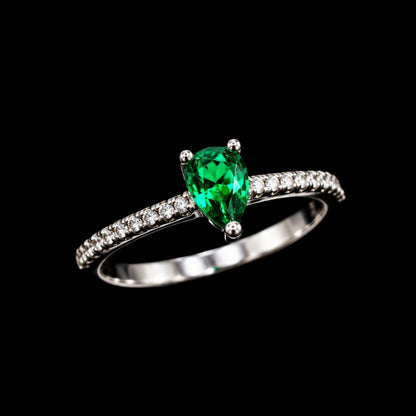A silver-tone ring with a pear-shaped emerald gemstone and CZ accents.